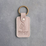 Gray sand leather keychain debossed with a pair of dog tags above the words Mustered out and JUNE 2026, on gray concrete
