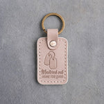 Gray sand leather keychain debossed with a pair of dog tags above the words Mustered out and HOME FOR GOOD, on gray concrete