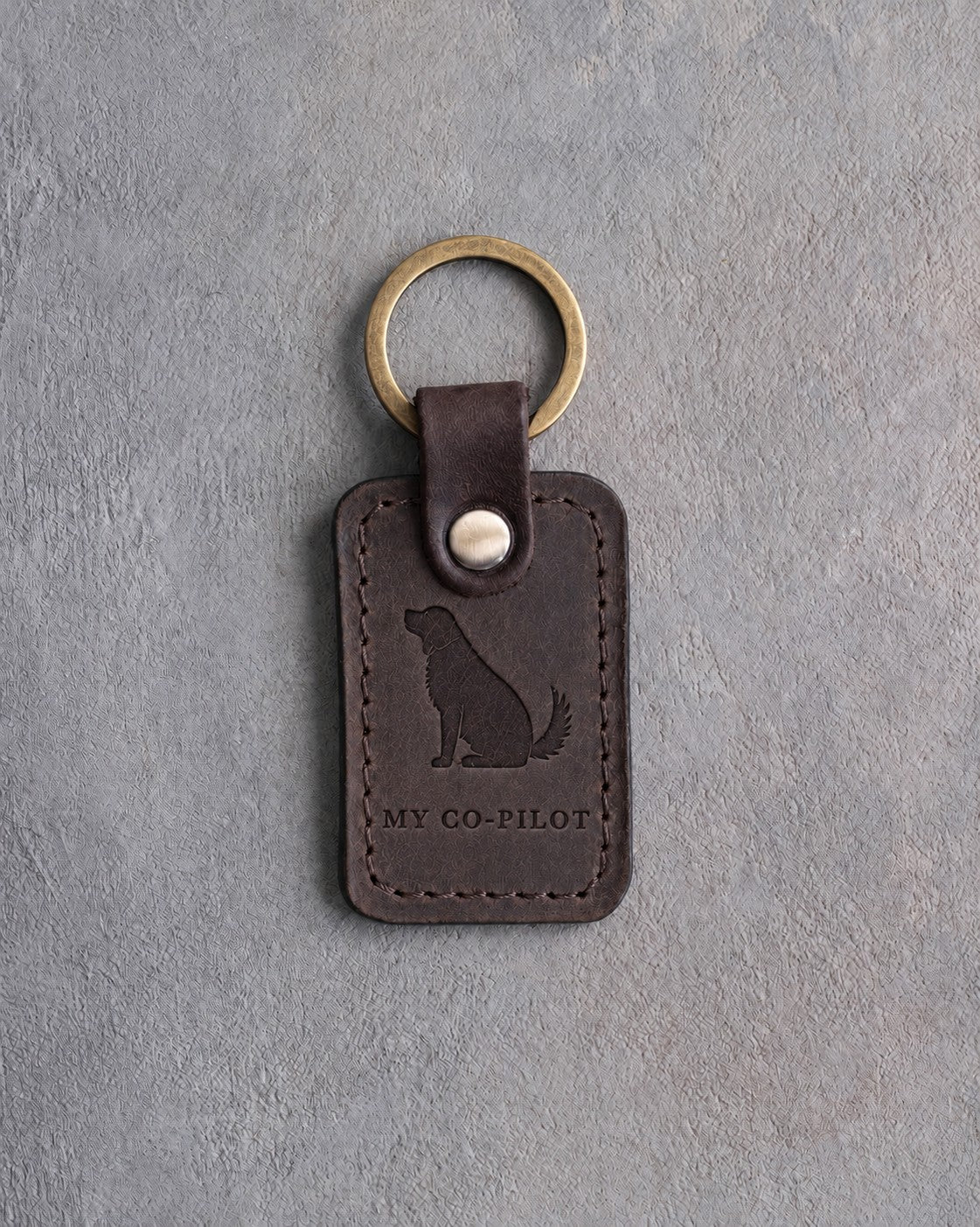 Dark espresso leather keychain debossed with a dog looking up above MY CO-PILOT, on gray concrete