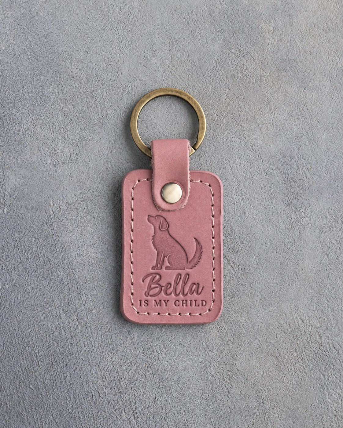 Parisian Blossom pink leather keychain debossed with a mutt looking up above Bella and IS MY CHILD, on gray concrete
