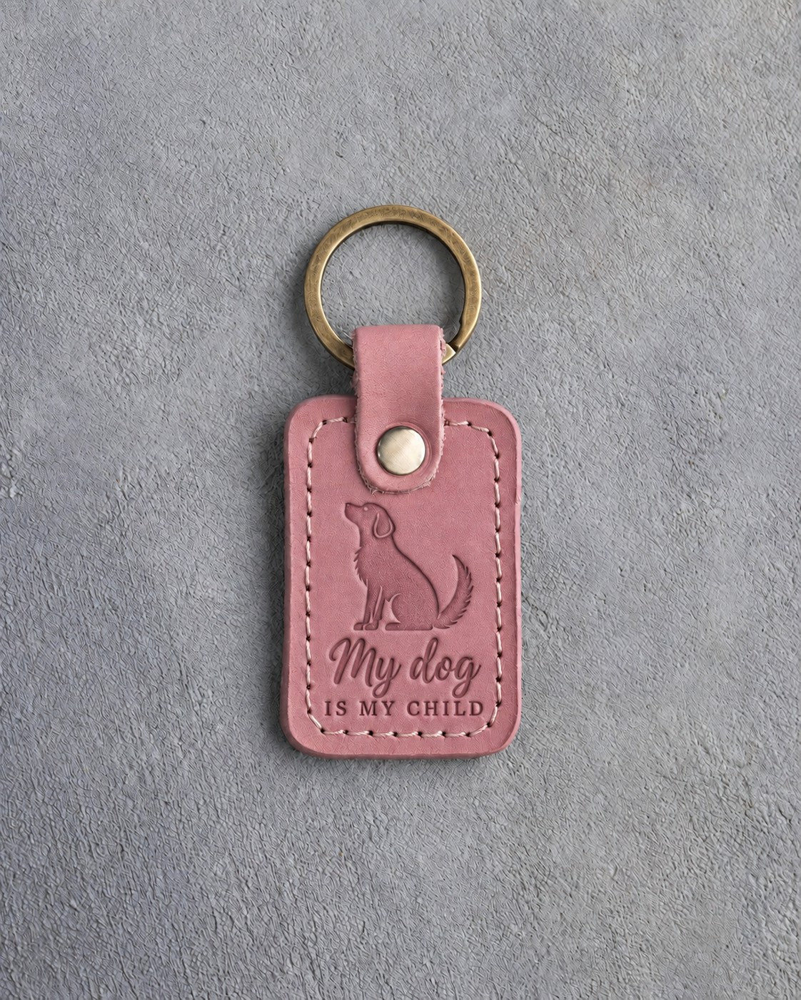 Parisian Blossom pink leather keychain debossed with a mutt looking up above My dog and IS MY CHILD, on gray concrete