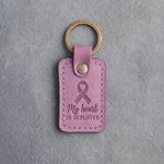 Lilac leather keychain debossed with a looped ribbon above the words My heart IS DEPLOYED, on gray concrete