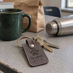 My Patients Bite keychain in gray leather on scrub pocket keys beside a coiled leash in a veterinary clinic