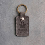 Country gray leather keychain debossed with a paw print above the words My patients and BITE, on gray plaster