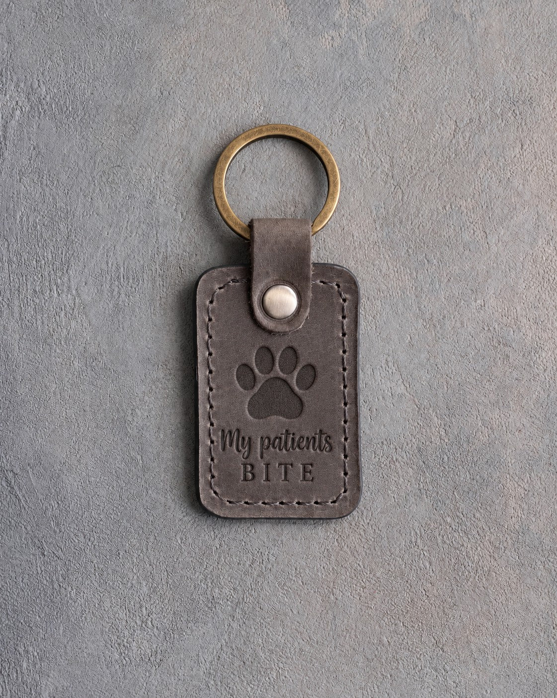 Country gray leather keychain debossed with a paw print above the words My patients and BITE, on gray plaster