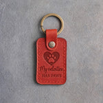 Poppy red leather keychain debossed with a heart holding a paw print above My valentine and HAS PAWS, on gray concrete