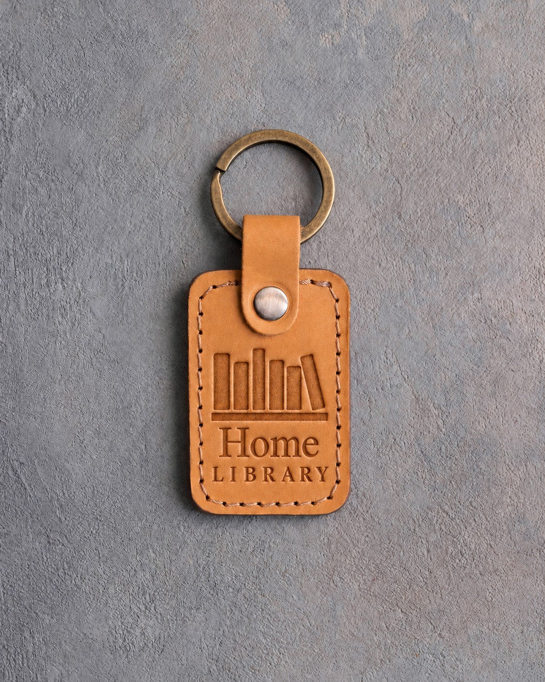 Indian Summer tan leather keychain debossed with a row of books on a shelf above Home and LIBRARY, on gray concrete