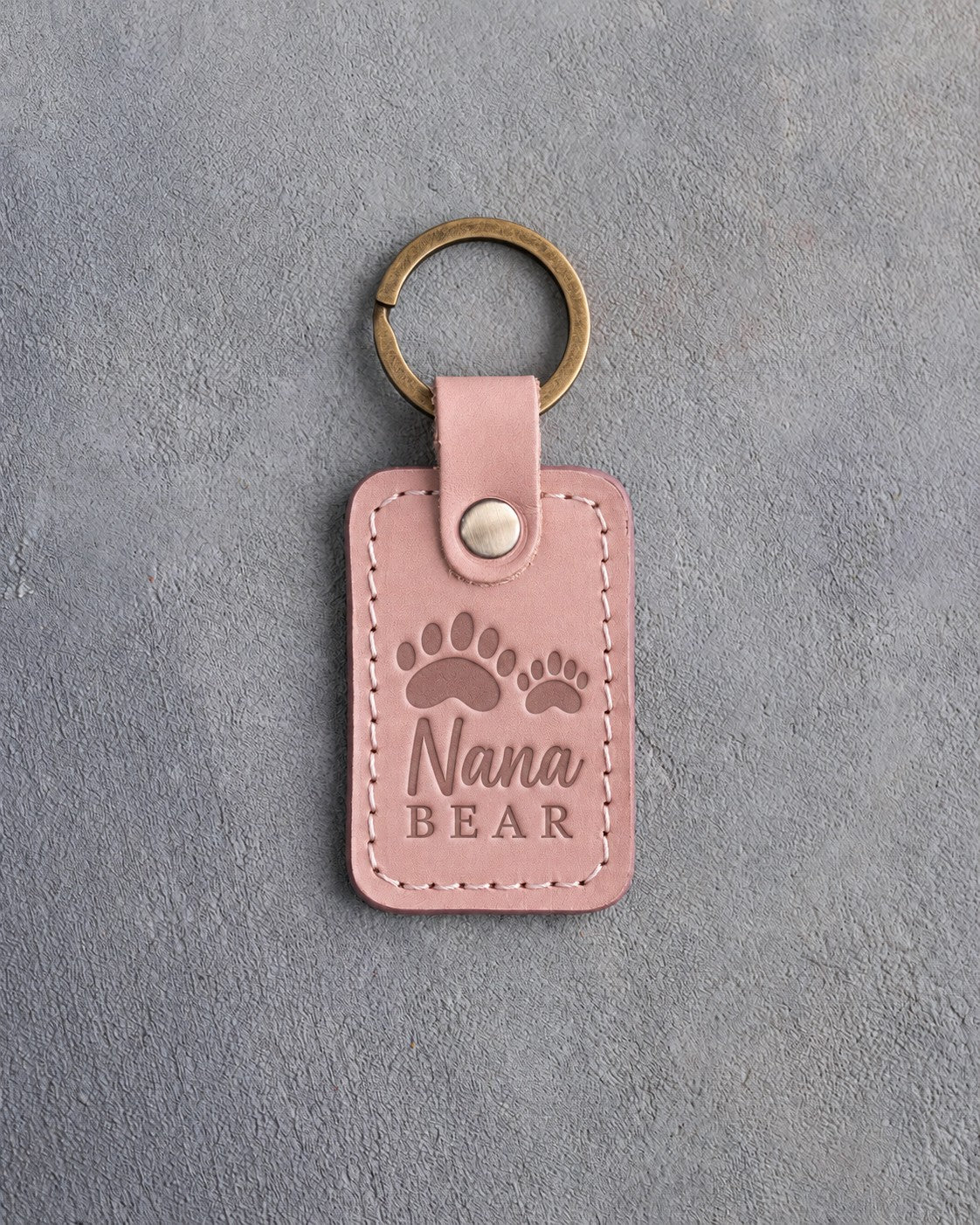 Blush pink leather keychain debossed with a large bear track and a small cub track above the words Nana BEAR, on gray plaster