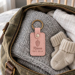 Blush Nana EST 2026 keychain resting on a sonogram card on a wooden table