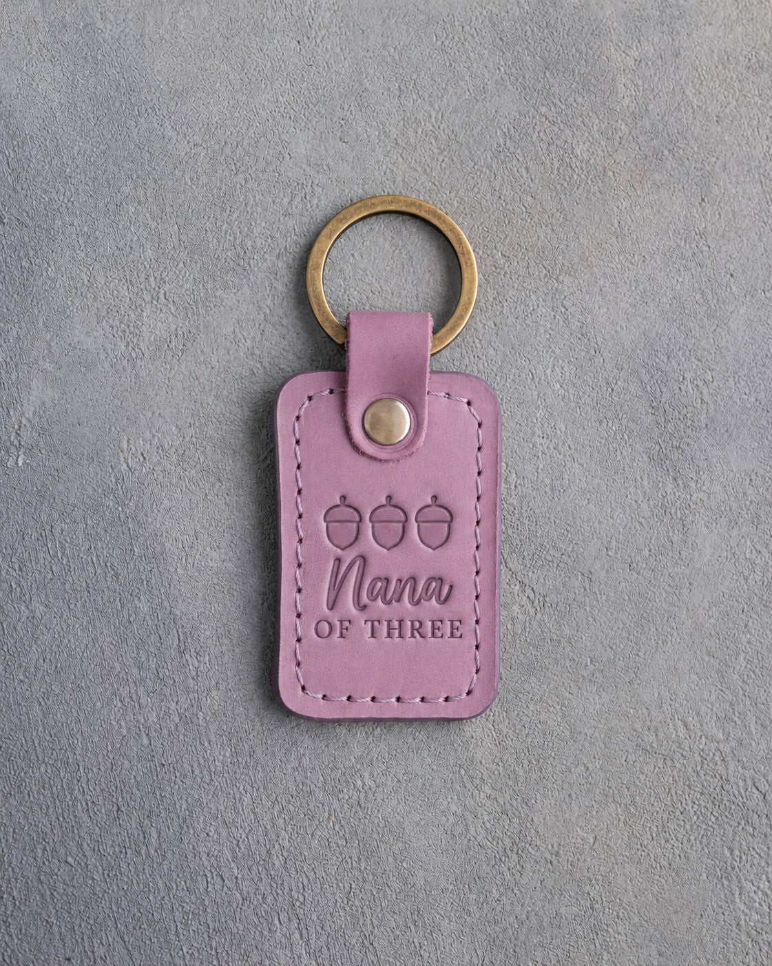 Lilac leather keychain debossed with a row of three acorns above Nana and OF THREE