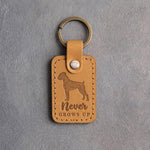 Indian Summer tan leather keychain debossed with a boxer silhouette and the words Never GROWS UP, on gray concrete