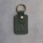 Forest green leather keychain with a debossed golden retriever and the phrase Never met A STRANGER on gray concrete