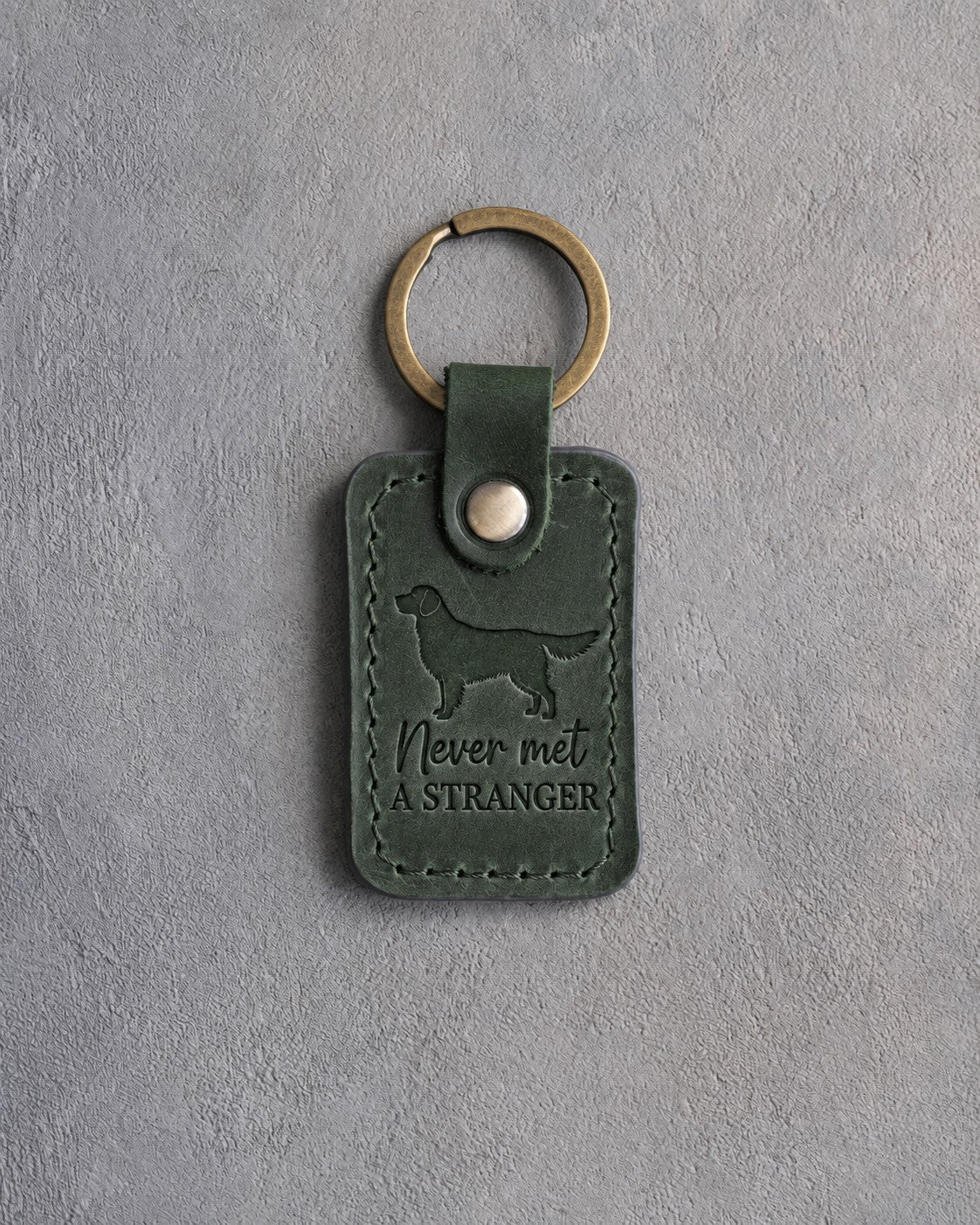 Forest green leather keychain with a debossed golden retriever and the phrase Never met A STRANGER on gray concrete