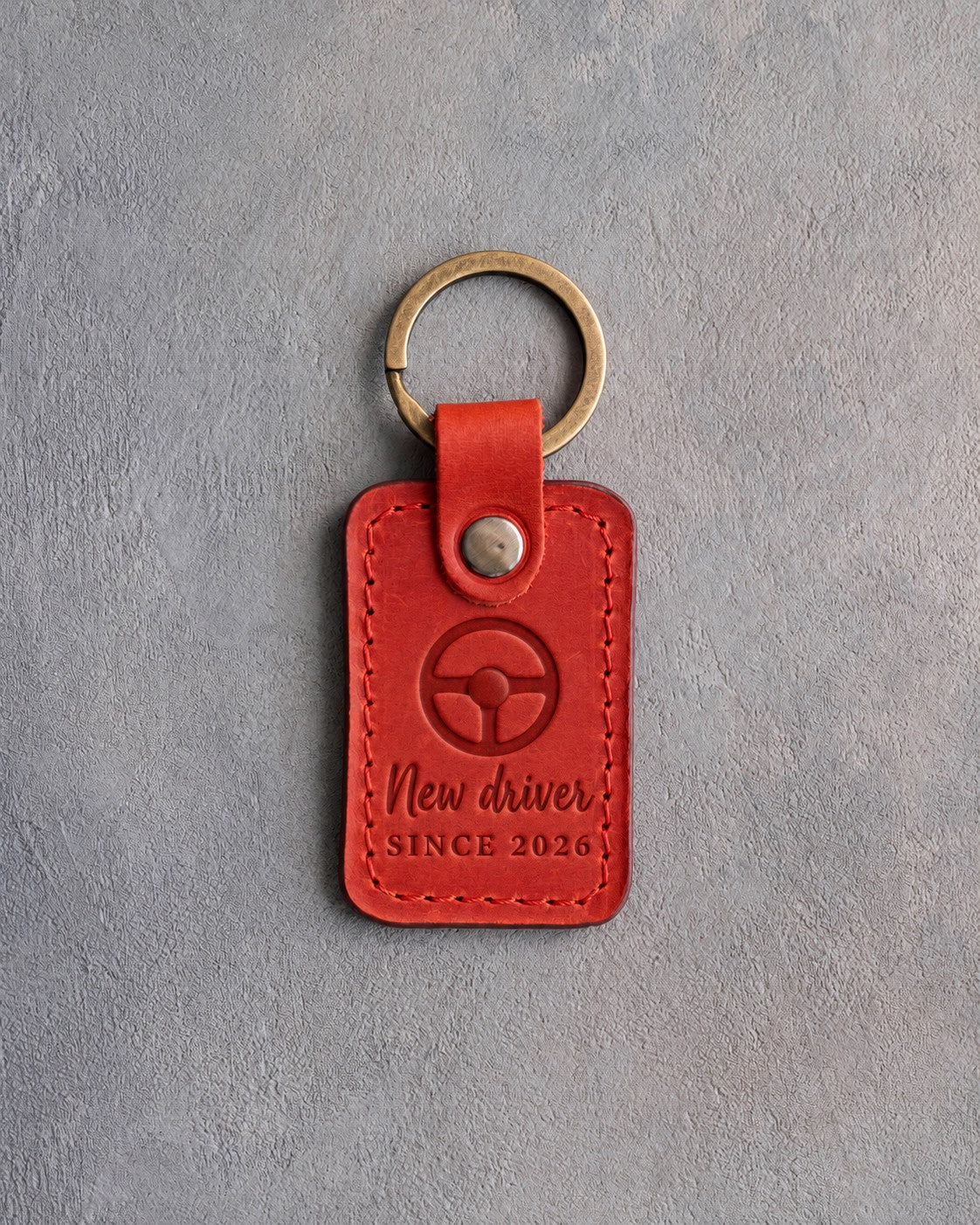 Poppy red leather keychain debossed with a steering wheel above New driver and SINCE 2026