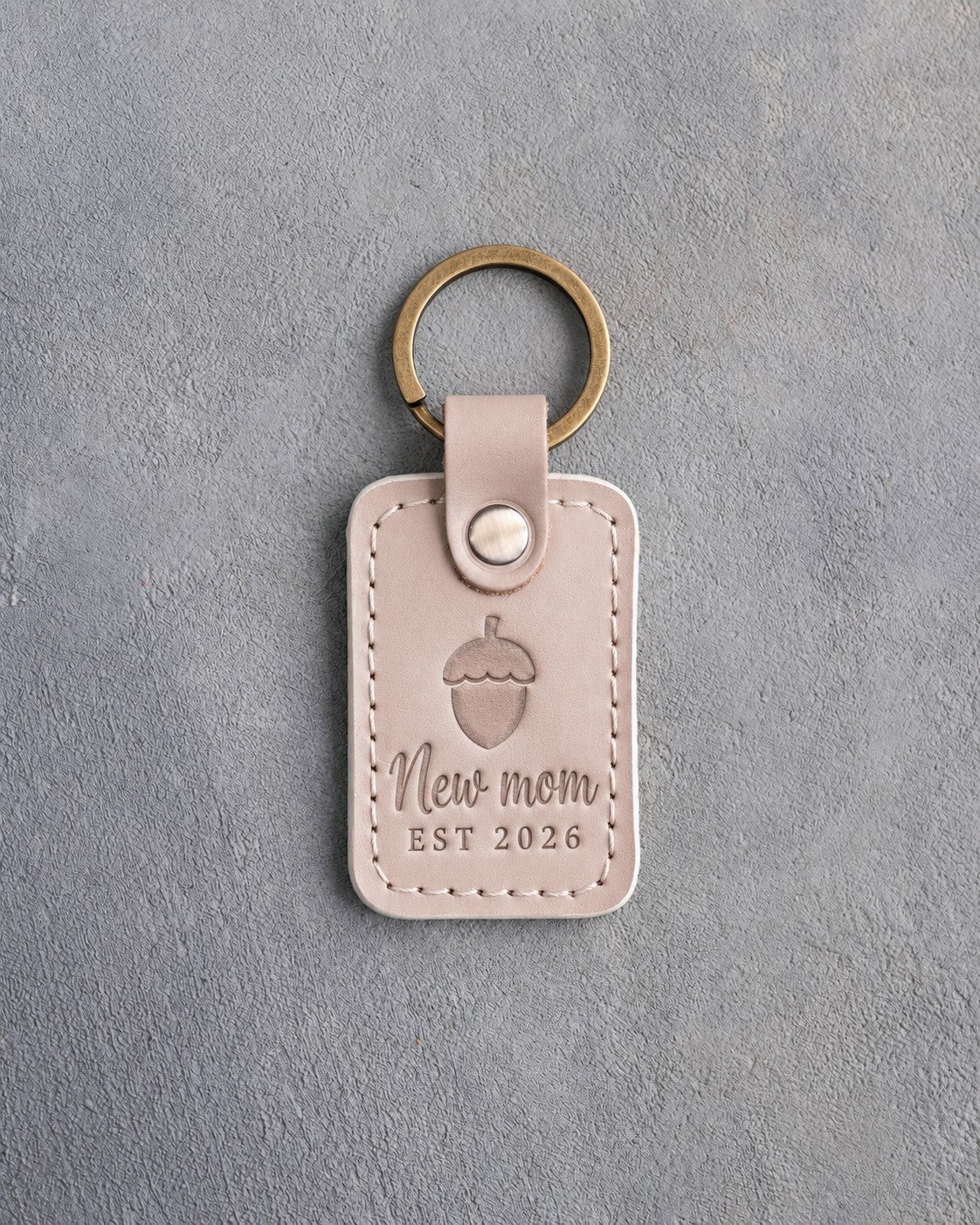 Gray sand leather keychain debossed with a single acorn above New mom and EST 2026