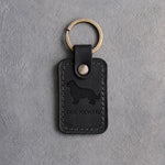 Black leather keychain debossed with a Newfoundland above THE NEWFIE, on gray concrete