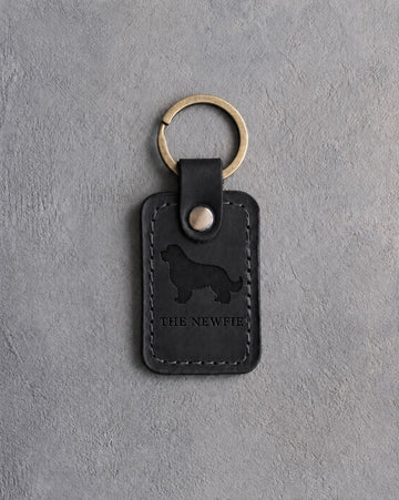 Black leather keychain debossed with a Newfoundland above THE NEWFIE, on gray concrete