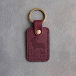 Sangria leather keychain debossed with a corgi in a Santa hat above Nice list and MILO · 2026, on gray concrete