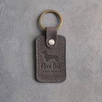 Country gray leather keychain debossed with a dachshund silhouette and the words Nice list UNDER REVIEW, on gray concrete