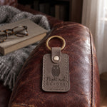 Gray Night owl READER keychain on a bedside table beside a book light and a thick novel