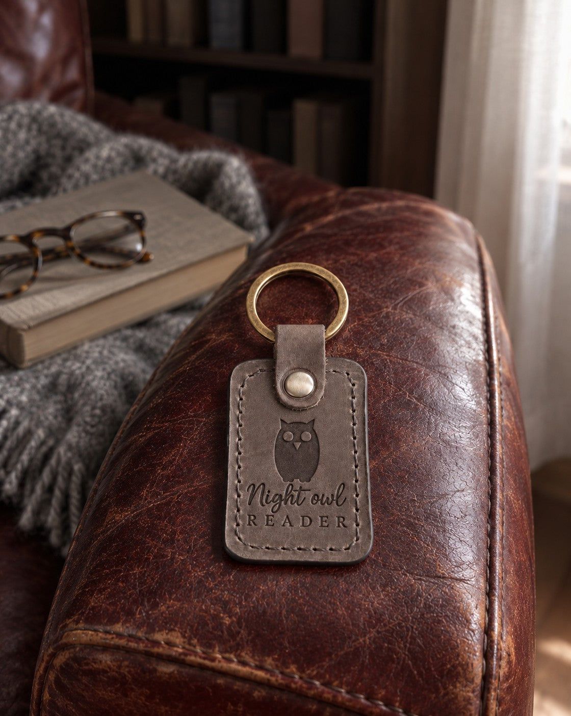 Gray Night owl READER keychain on a bedside table beside a book light and a thick novel