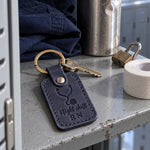 Night Shift RN keychain in navy leather on a lanyard of hospital badge keys resting on a dark kitchen counter at dawn