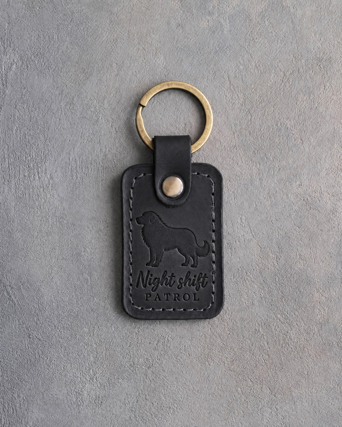 Black leather keychain debossed with a Great Pyrenees and the words Night shift PATROL, on gray concrete