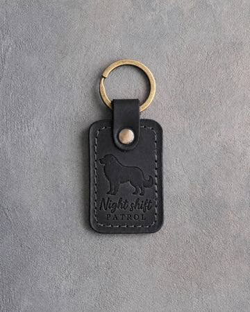 Black leather keychain debossed with a Great Pyrenees and the words Night shift PATROL, on gray concrete