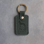 Forest green leather keychain debossed with a Belgian Malinois and the words No off SWITCH, on gray concrete