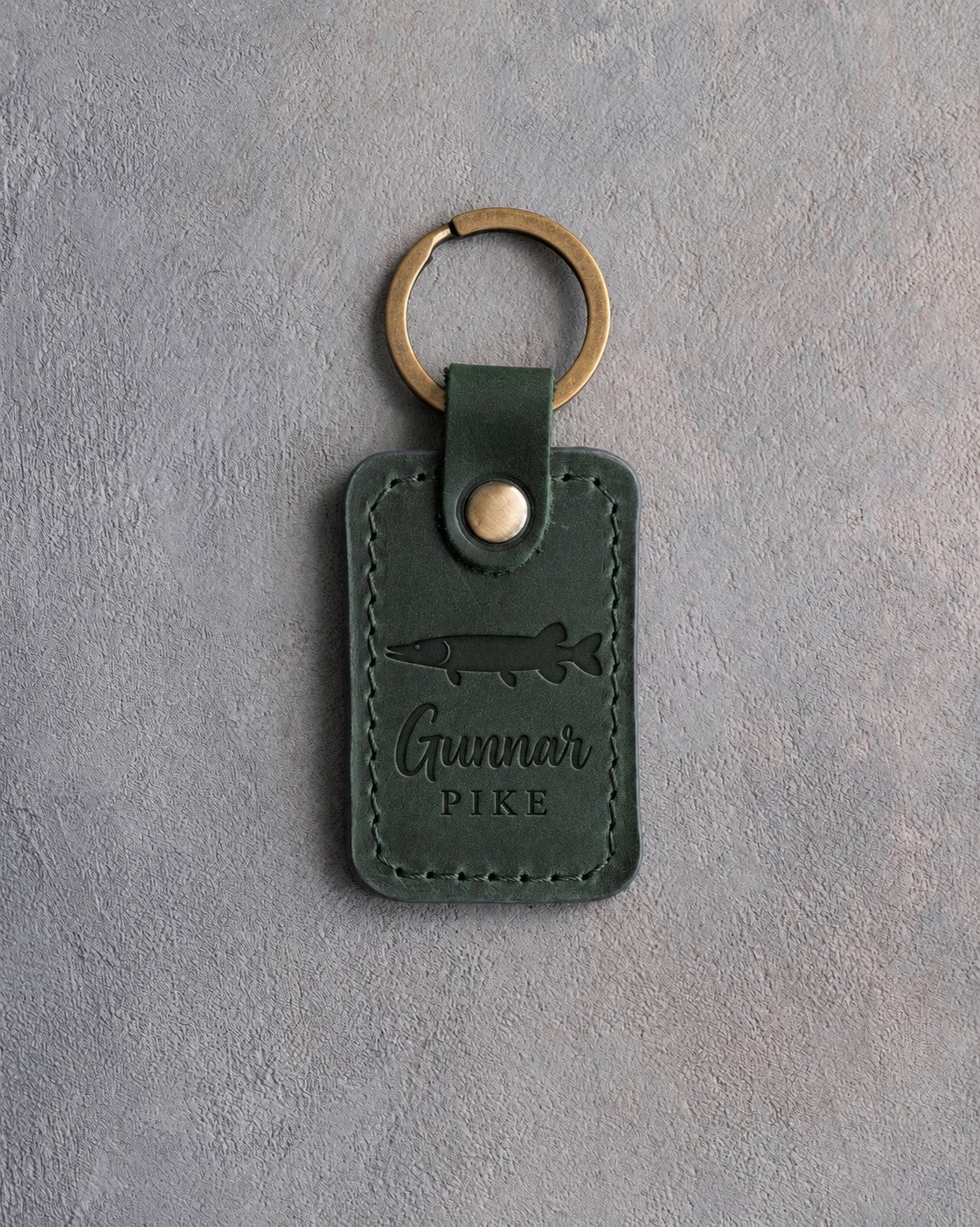 Forest Green leather keychain debossed with a northern pike above Gunnar and PIKE, on gray plaster