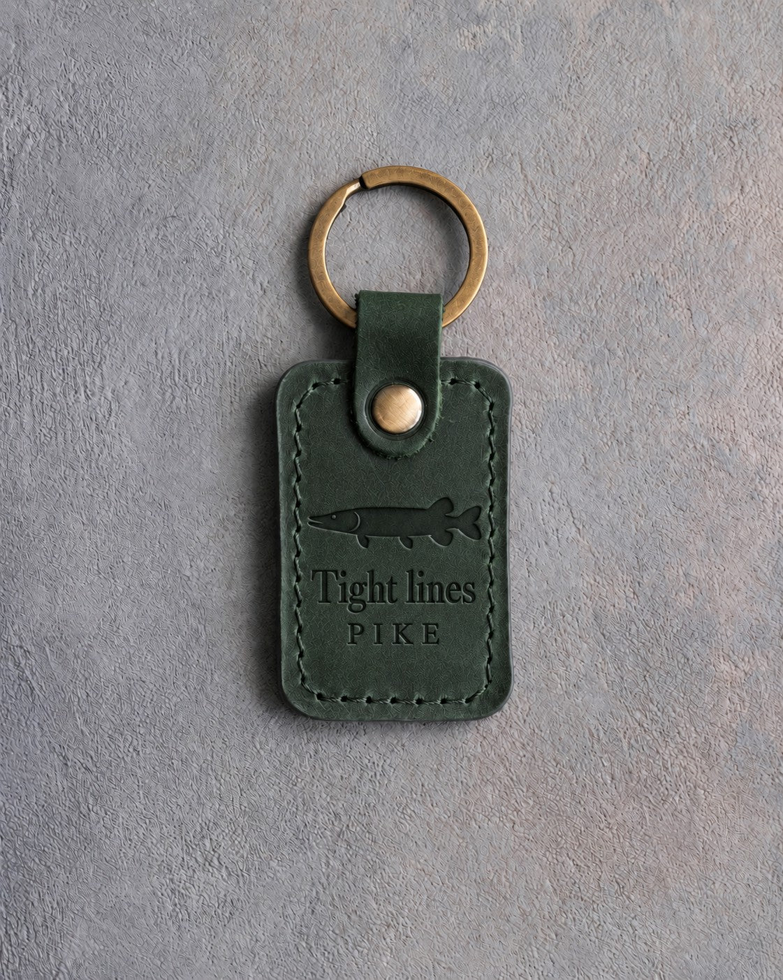 Forest Green leather keychain debossed with a northern pike above Tight lines and PIKE, on gray concrete