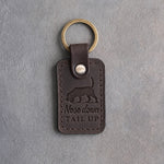 Dark espresso leather keychain debossed with a beagle trailing a scent with its tail up and the words Nose down TAIL UP, on gray concrete
