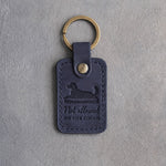 Blueberry navy leather keychain debossed with a dog lying on a sofa cushion and the words Not allowed ON THE COUCH, on gray concrete