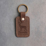 Sicilian brown leather keychain debossed with a whitetail buck above the words November IS FOR BUCKS, on gray plaster
