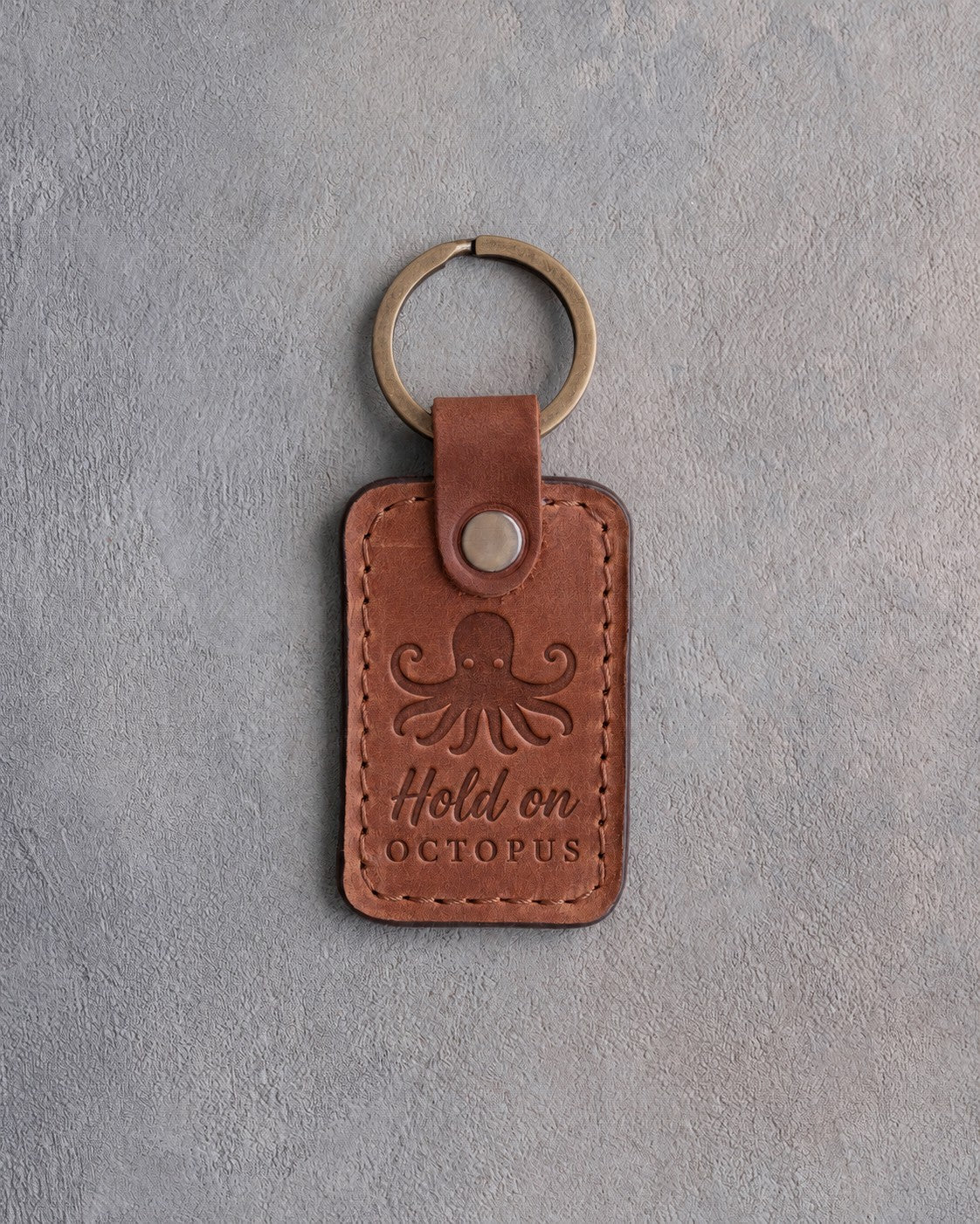 Arizona leather keychain debossed with an octopus above Hold on and OCTOPUS, on gray plaster