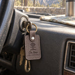 Gray On Time Yellowstone keychain clipped to a camera strap on a wooden boardwalk under a wide sky