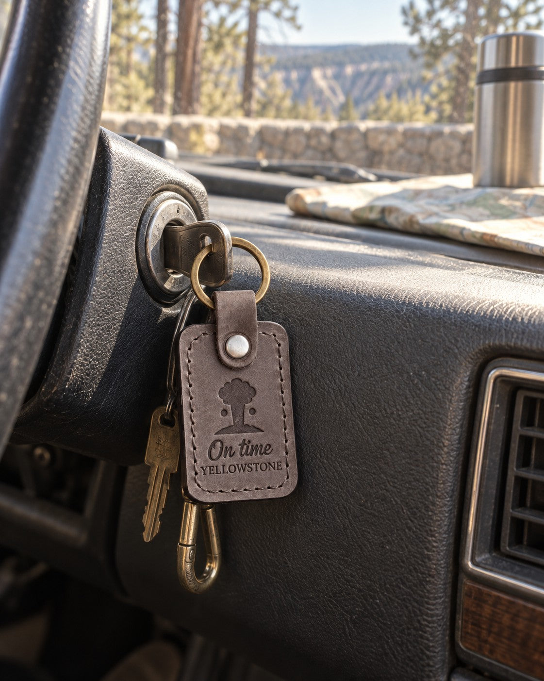 Gray On Time Yellowstone keychain clipped to a camera strap on a wooden boardwalk under a wide sky