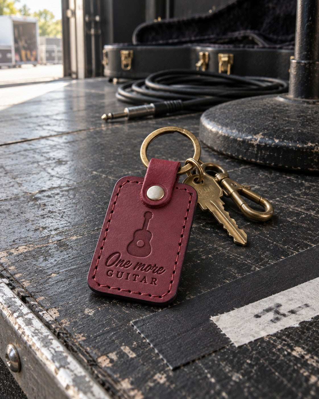 One More Guitar keychain in wine red leather on a house key hanging beside a wall of hung guitars