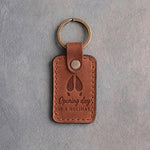 Warm tan leather keychain debossed with a whitetail deer track above the words Opening day IS A HOLIDAY, on gray plaster
