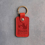 Poppy red leather keychain debossed with a cat knocking a Christmas bauble off its paw above the words Ornament ON THE FLOOR