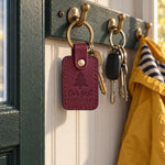 Wine red Our first CHRISTMAS keychain hanging from a branch of a small Christmas tree