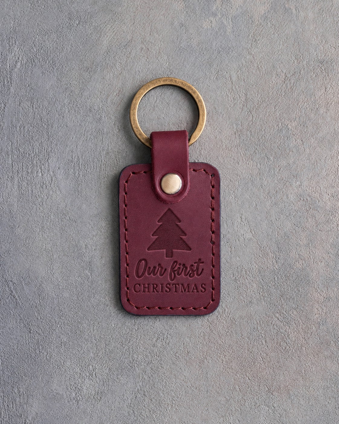 Sangria red leather keychain debossed with a three-tier fir tree above Our first and CHRISTMAS