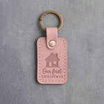 Blush pink leather keychain debossed with a gable-front house above Our first and CHRISTMAS, on gray concrete