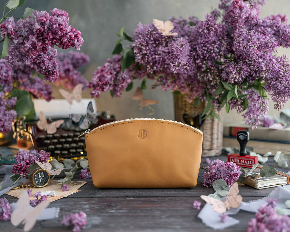 Personalized makeup bag in indian summer golden-tan leather with a small gold monogram, lilacs behind