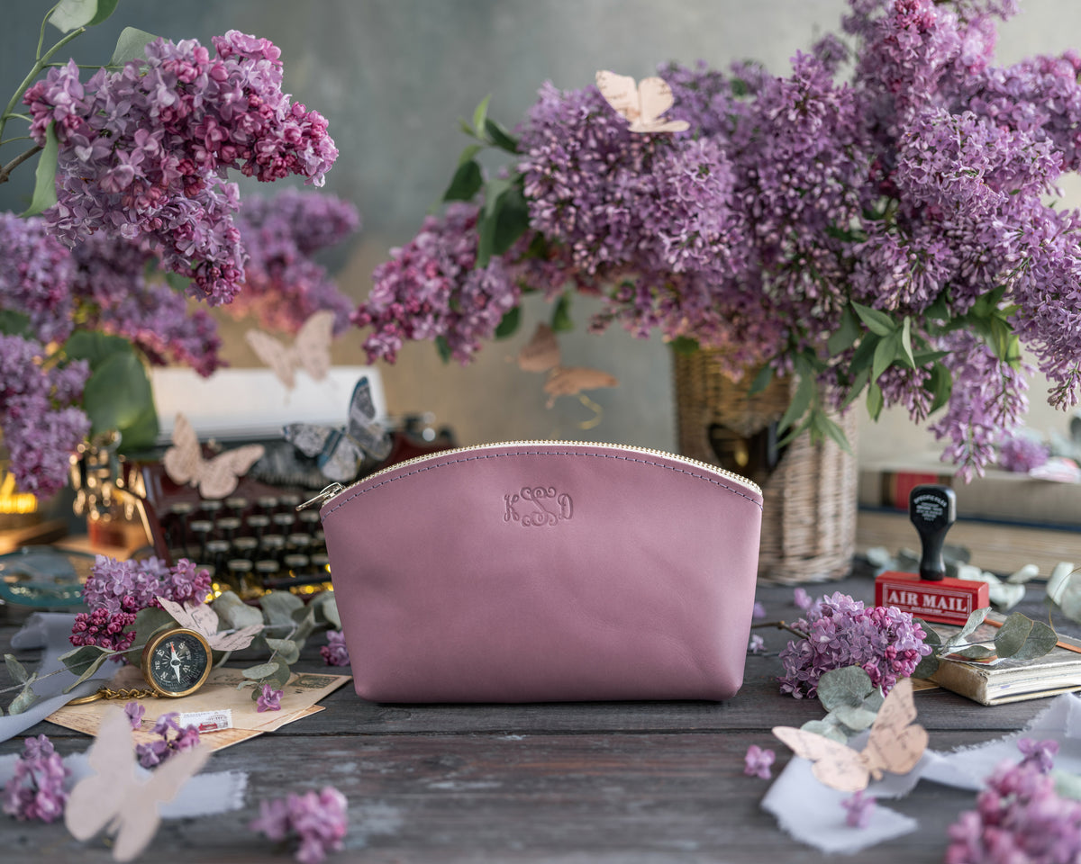Lilac leather makeup pouch with a delicate gold monogram, matching purple lilacs behind
