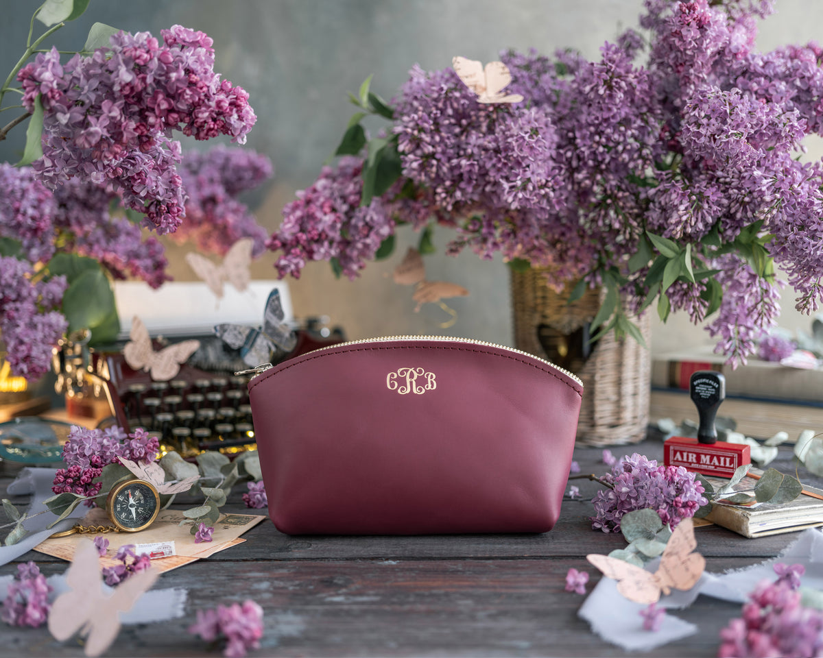 Sangria burgundy leather makeup pouch with a cursive gold monogram, lilac blooms around