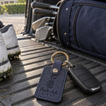 Packs Clubs First keychain in navy leather on car keys resting on a golf travel bag in an open trunk
