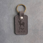 Country gray leather keychain debossed with a Papillon silhouette and the words Pap DAD, on gray concrete