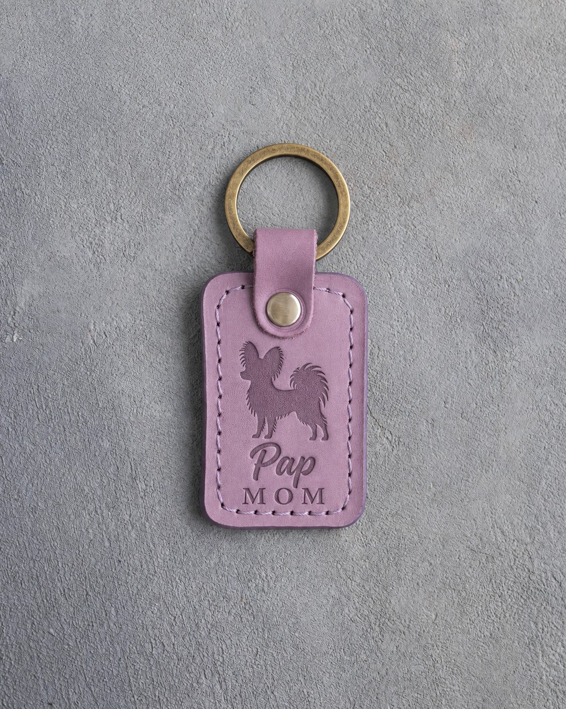 Lilac leather keychain debossed with a Papillon silhouette and the words Pap MOM, on gray concrete