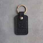 Black leather keychain blind debossed with a five-pointed star badge and the words Partner K9 UNIT, on gray concrete